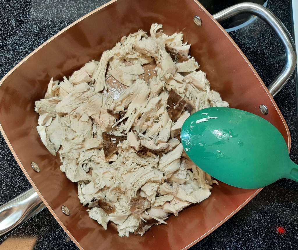 cooked, shredded or cut up pieces of turkey in square copper pan with teal cooking spoon