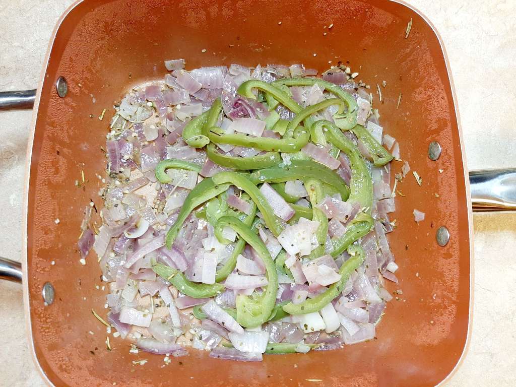 sliced green bell peppers and sliced red onions cooking in square pan