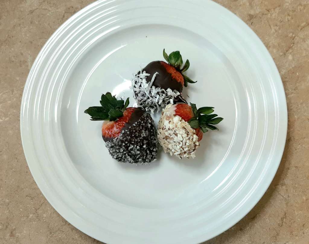 3 decorated chocolate covered strawberries on a white plate
