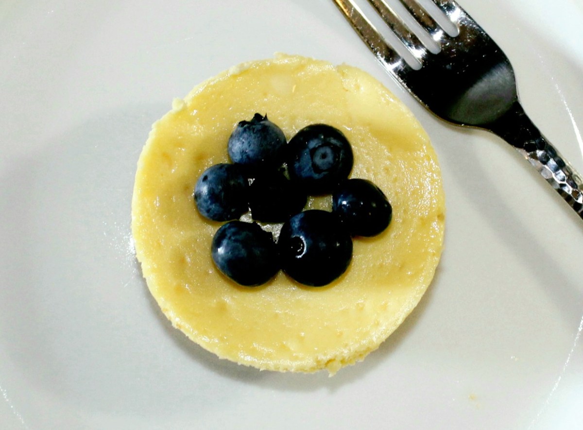 small round mini cheesecake with 7 blueberries clustered on top in the center of it on a white plate
