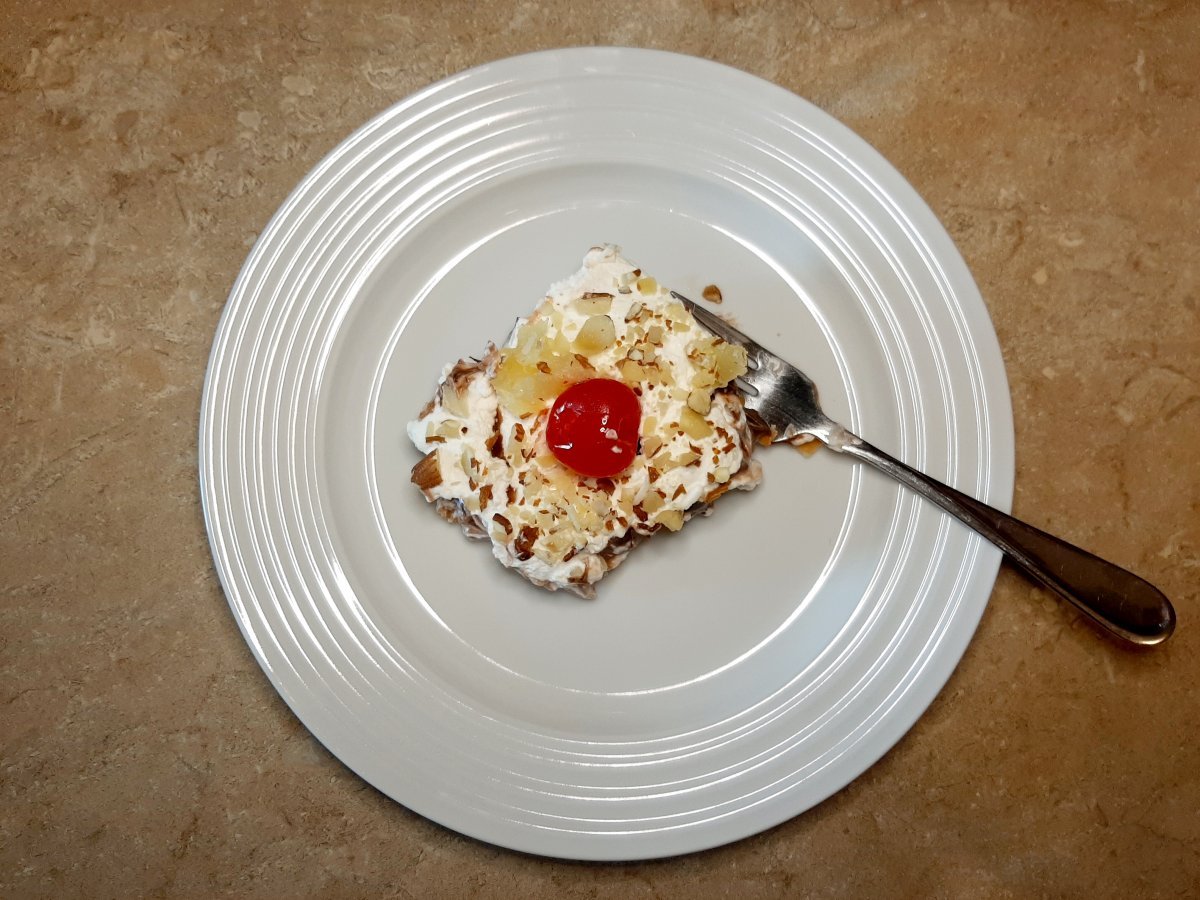 slice of banana pineapple cream cheese dessert with whipped cream, pineapple, and a cherry on a white plate