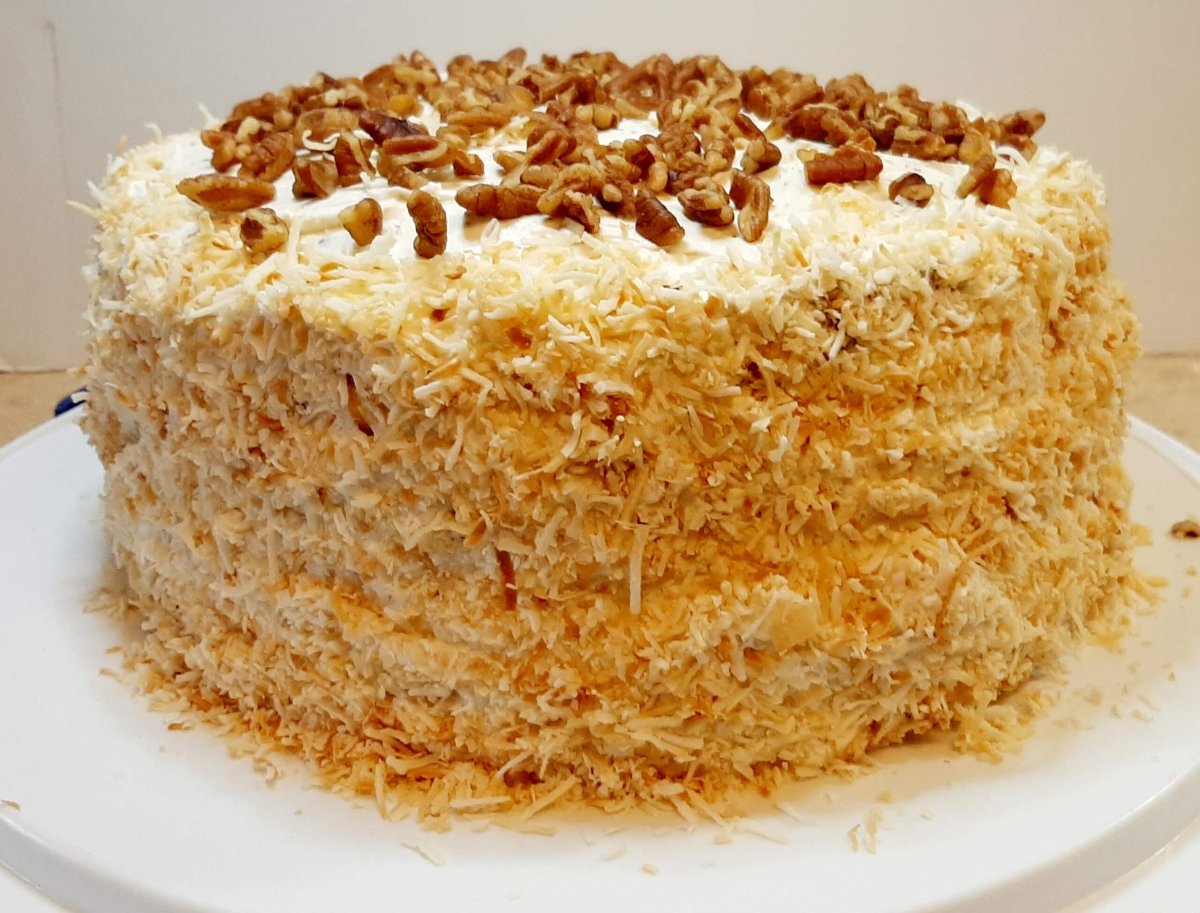 Italian Cream Cake on white platter with coconut and pecans on creamy frosting