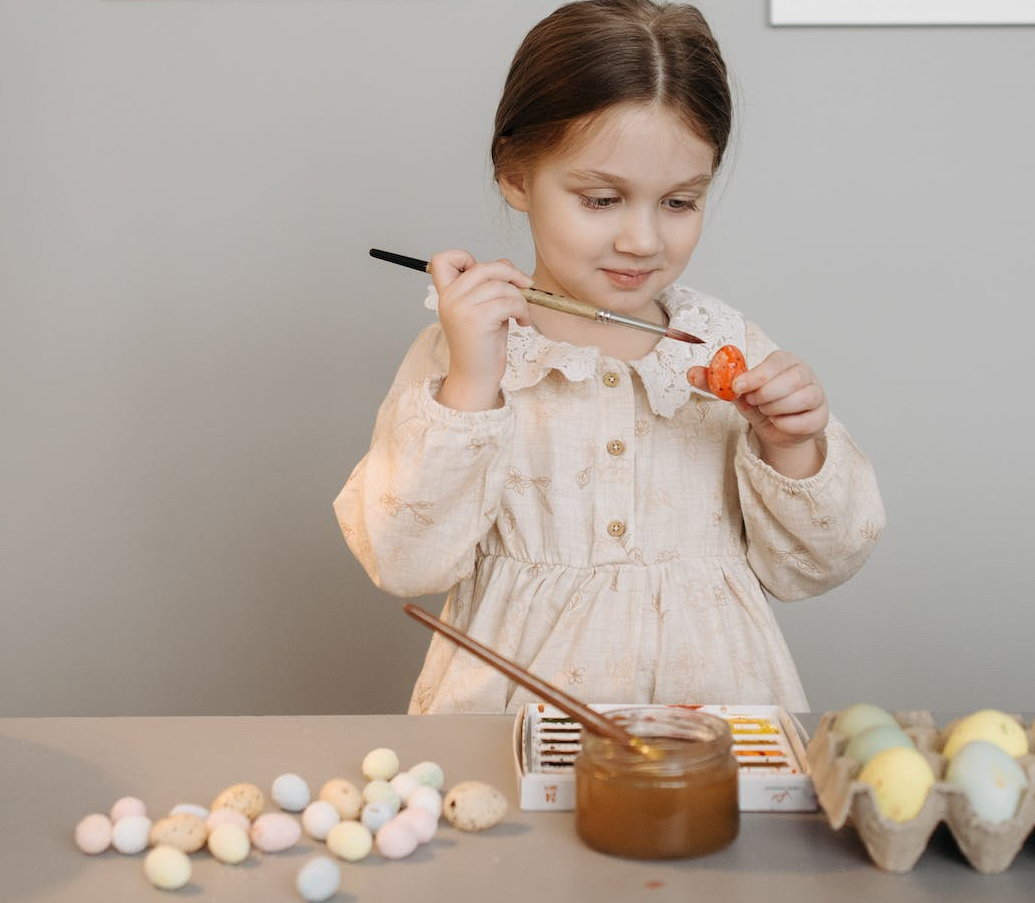 photo of a kid decorating an easter egg near a lamp