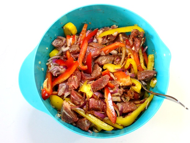 cut up beef, bell peppers, and onions marinating in a turquoise bowl