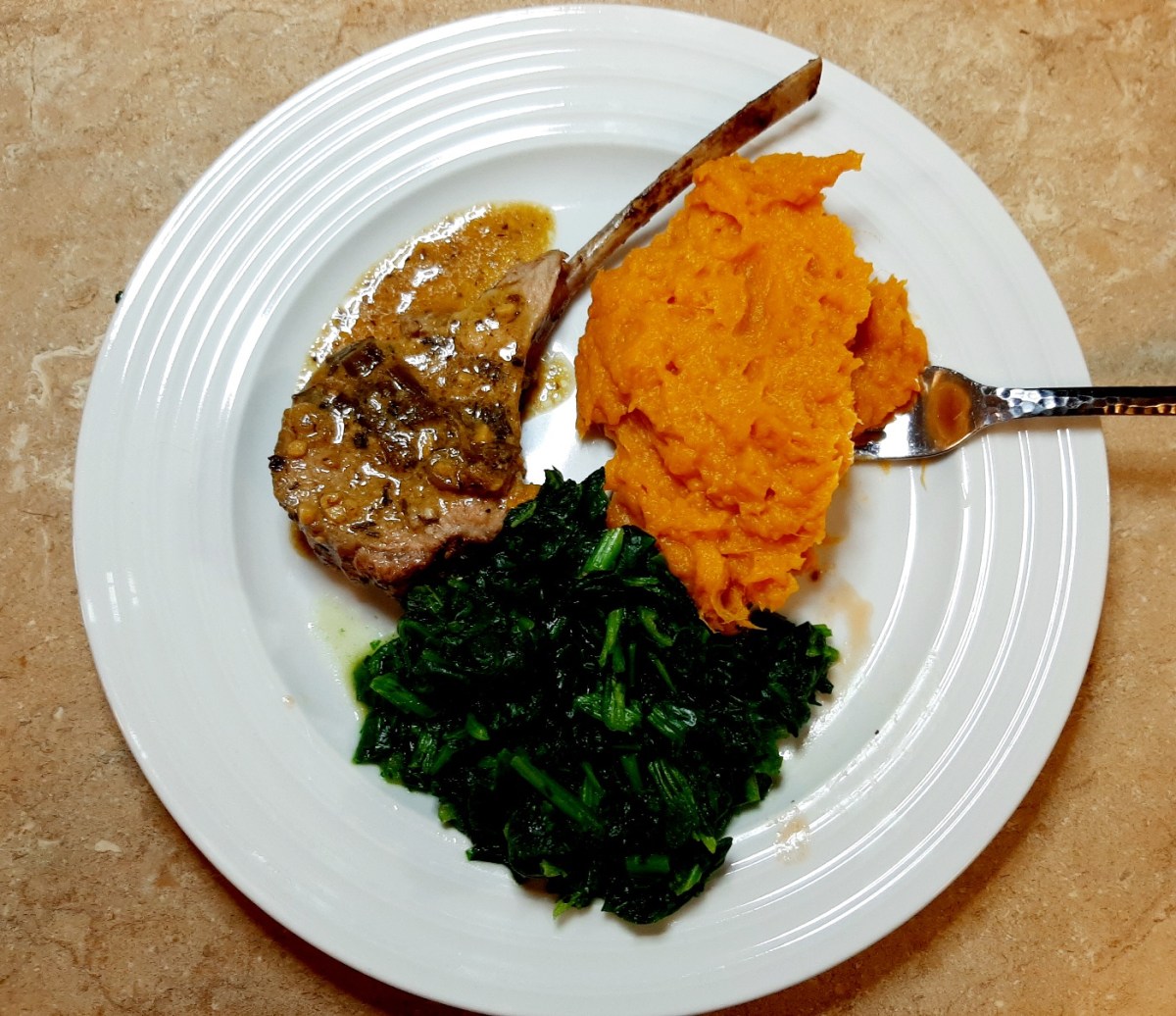 lamb chop with sauce on it, spinach, and mashed sweet potatoes on a white plate
