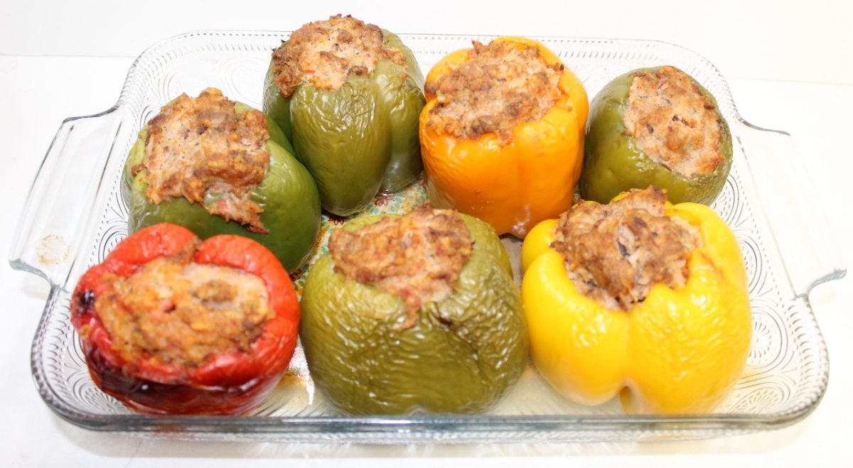 green, yellow, and red stuffed bell peppers in a clear baking dish on white background