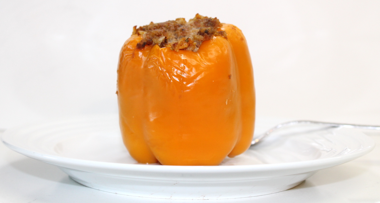 cooked orange stuffed bell pepper on white plate on white background