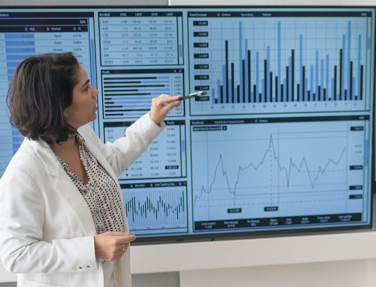 woman in white suit discussing stock market data to her colleagues