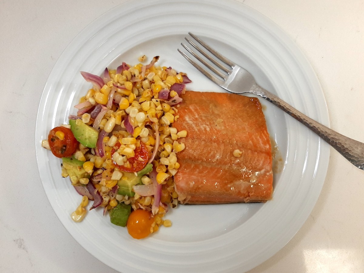 cooked salmon fillet with a salad made of cooked whole kernel corn, sliced red onion, cherry tomatoes, and diced avocado
