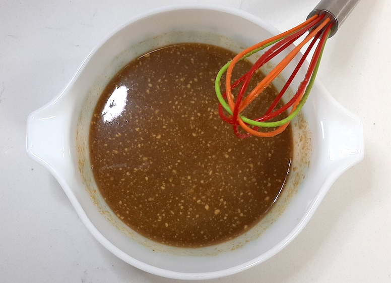 brown sauce or grave with seasoning in a small round casserole dish and a multi colored whisk propped on it