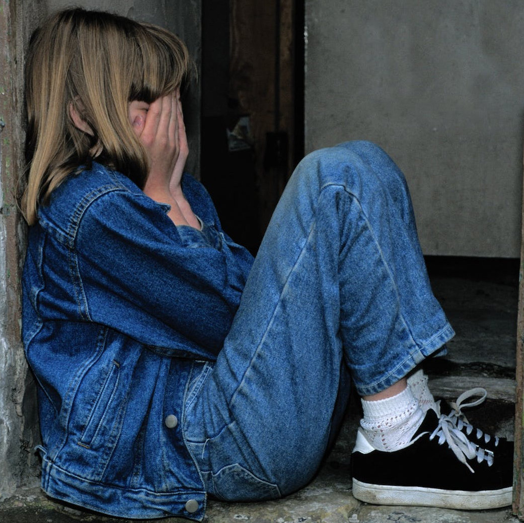 girl in denim sitting alone crying in a doorway