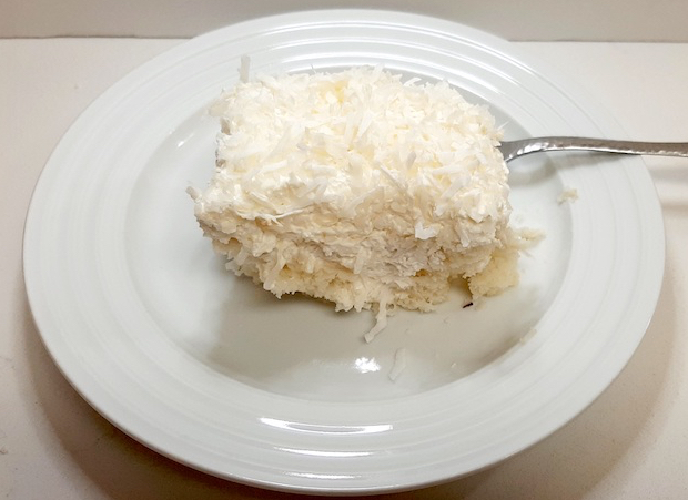 Slice of white cake topped with flake coconut on a white plate