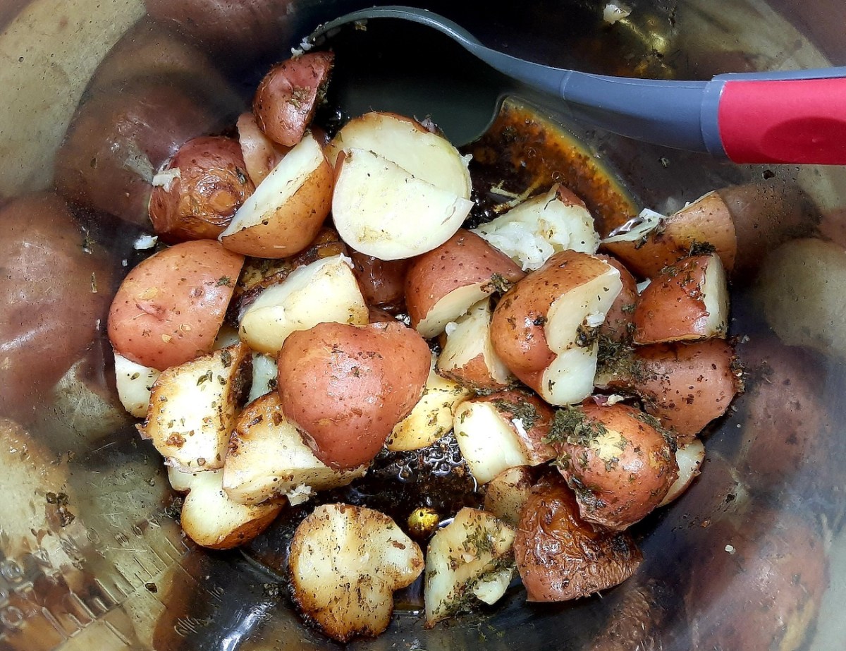 cooked, quartered, and seasoned new potatoes in a metal bowl with a plastic gray and red serving spoon
