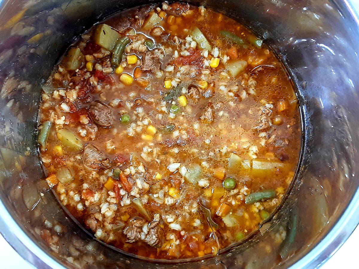top down view of cooked vegetables, meat, potatoes, and liquid in a pot