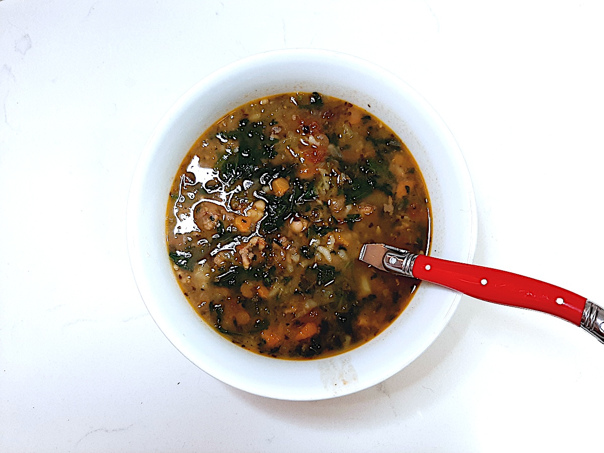 white bowl of soup with different kinds of cooked beans, tomatoes, rice, and carrots on a white background